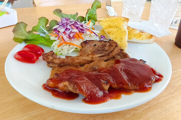 Delectable Pork Steak Delight: A close-up captures a mouthwatering pork steak, smothered in rich sauce, artfully plated with fresh salad, tomatoes, and crispy garlic bread.