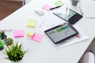 ESG report on tablet with office desk, sticky notes and charts, modern workspace showing sustainability metrics and focused collaboration