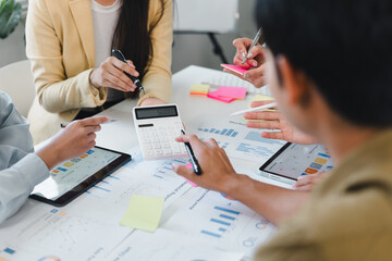 Small business team analyzing financial chart with calculator and tablet, collaborative meeting with charts and sticky notes expressing focused