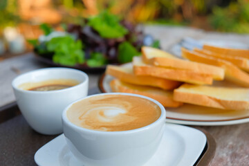 a cozy breakfast setting at a window table. a cup of coffee sits alongside a plate of sliced bread topped with butter, suggesting a simple yet comforting morning meal