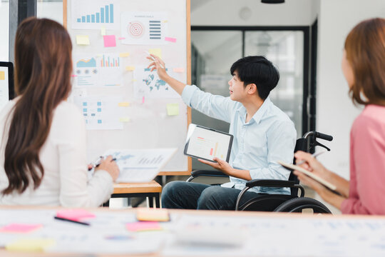 Young man in wheelchair leading business meeting disability teamwork presentation tablet chart board