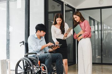 Young man in wheelchair collaborating with two colleagues in modern office disability teamwork meeting technology inclusion