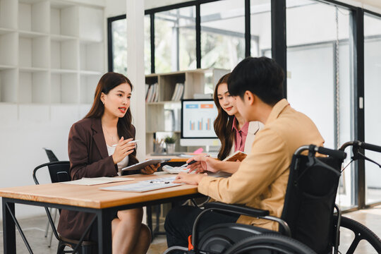 Young professional team meeting with colleague in wheelchair discussing documents and inclusive planning with supportive expression disability