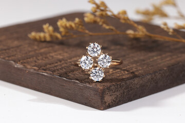 Elegant gold ring featuring four round-cut diamonds arranged in a floral cluster design, displayed on a wooden surface.