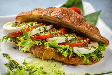 Fresh croissant sandwich with mozzarella, tomato and pesto