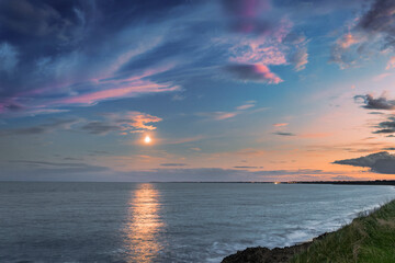 Coastal evening panorama of moonlit sea, twilight clouds in pink and blue, serene Irish shoreline