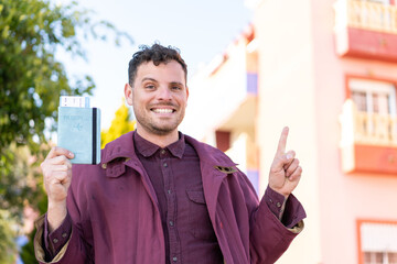 Young caucasian man holding a passport at outdoors pointing to the side to present a product