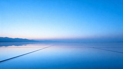A serene, expansive view of a calm lake reflecting the clear blue sky with distant mountains on the horizon.
