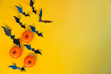 Flying black bats and pumpkins on yellow background. Festive Halloween design with copy space for...