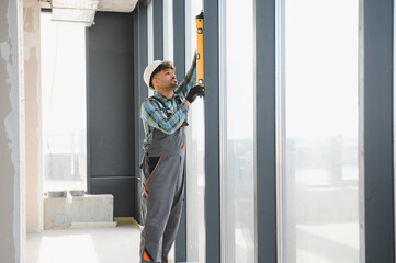 Construction worker using spirit level on window frame in building under construction