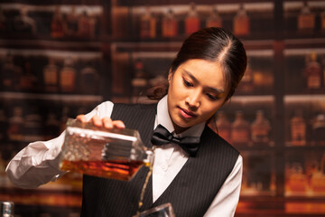 Bartender woman pours whiskey into a glass in a restaurant.	