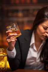 Asian woman in a black suit sitting holding a glass of whiskey at night in a restaurant.	