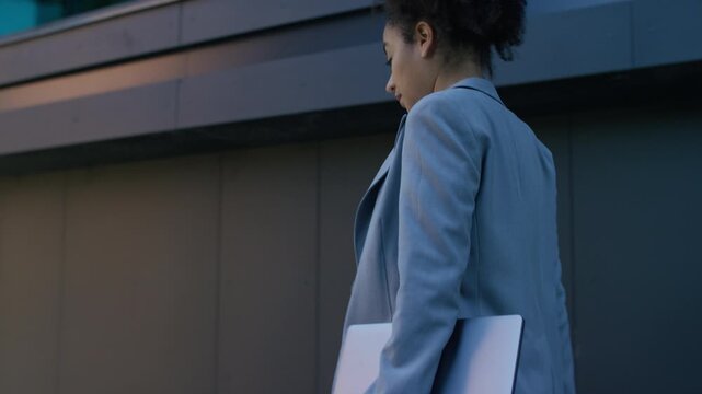 Confident businesswoman walking with laptop in hand