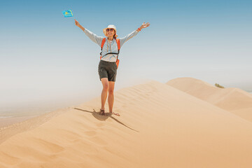 Female tourist waving Kazakhstan flag while walking in Singing Barkhan desert, inside Altyn Emel National Park, during summer sunny day