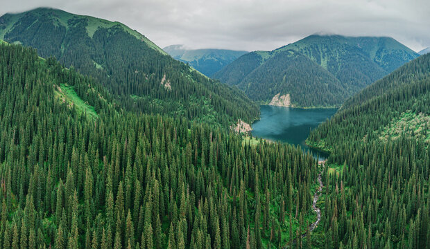 Aerial view of coniferous forests covering mountain slopes surrounding Kolsai Lakes in Kazakhstan under cloudy sky - Powered by Adobe
