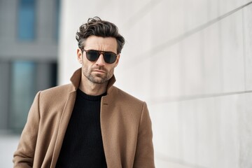 Fototapeta premium stylish man in tailored wool coat, sunglasses, neutral tones outfit, clean modern background, quiet luxury fashion