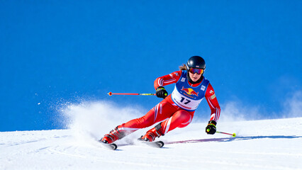 Skier in action during a downhill race on a snowy slope under clear blue sky