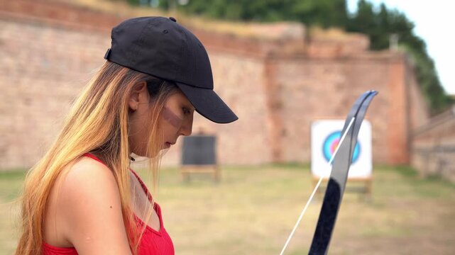 Concentrated young woman practicing archery. Focused archer aiming with bow and arrow at an outdoor shooting range with a target
