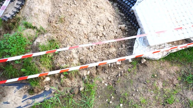 Safety first concept with red and white striped caution tape marking a hazardous dug-up area on a construction site