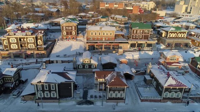 Flight sideways historic 130 Quarter district, Irkutsk, Russia. Winter sunset over wooden log houses, slavic architecture, Snowy roofs, carved shutters. Golden hour scenic village. Travel landmark