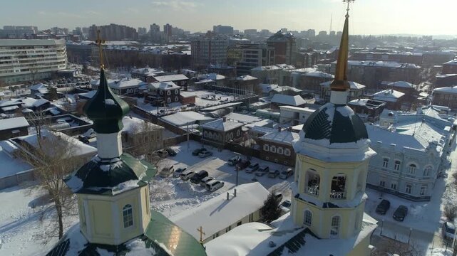 Aerial forward over a snowy ancient Russian village. Old Slavonic style church with domes and historic izba wooden houses in Irkutsk. 130 Kvartal district, winter, authentic old Russia atmosphere. 4k