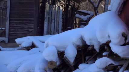Atmospheric winter abandoned courtyard among old wooden log houses. Authentic Slavic rural izba with poverty details, trash scattered in snow. Evokes decaying past, melancholic mood of forgotten place
