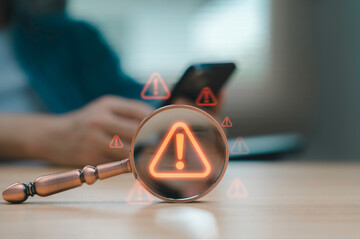 Magnifying glass focusing on warning alert icon with exclamation mark while businessman using smartphone Concept of cyber security data risk system error online fraud technology danger and caution