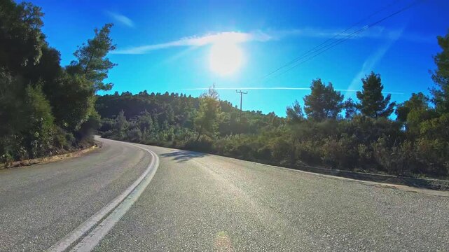 POV drive car travel curvy road green trees nature blue sky shining sun horizon