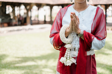 A person in traditional Thai clothing performs a respectful greeting with a floral garland in a...