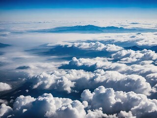 A stunning aerial view from above the clouds, with a beautiful blue sky and distant mountains in the background. The clouds form a thick, fluffy layer, creating a peaceful and serene atmosphere.