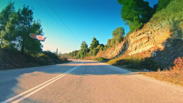 Green remote nature POV drive car travel, empty road, blue sky gleaming sun
