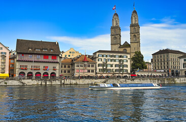 Obraz premium Zurich city center with famous Grossmunster churh and a tourist boat sails on the river Limmat, Switzerland