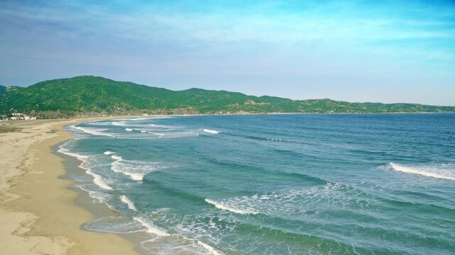 Seaside, coastal scenery panning, sandy beach waves washing ashore, blue sky