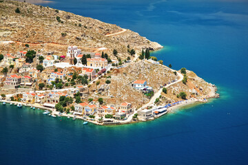 View of Ano Symi shore from a higher point, sun shines on traditional Mediterranean architecture building near sea