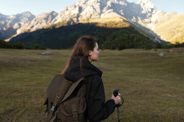 A lone hiker with a backpack gazes toward rugged mountains under a clear sky, capturing a moment of adventure and exploration in a vast alpine landscape. © SHOTPRIME STUDIO