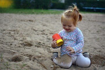 Joyful toddler girl sitting in a sandbox, laughing and playing with sand and colorful buckets, enjoying carefree childhood and outdoor playground fun.