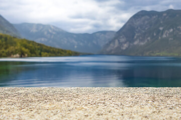 Obraz premium stone pedestal display on deep blue lake and mountain range backdrop. beige stone empty podium against vibrant mountain landscape with