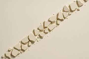 Minimal beige stone/plaster fragments in diagonal line on neutral background — top view