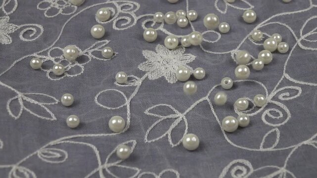 Pearl beads fall onto blue chiffon fabric with embroidered flowers, slow motion. Fashionable clothing design elements, background
