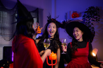 Fototapeta premium Excited young Asian women celebrating Halloween party, laughing and toasting drinks in spooky costumes