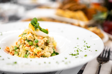 Traditional Russian Olivier salad served in a white bowl, garnished with egg and herbs. Classic festive dish with diced vegetables and creamy dressing, ideal for holiday food themes.