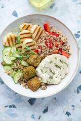 Halloumi cheese with quinoa, falafel and vegetables, vertical shot on a white and blue granite background, elevated view