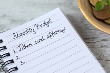Christian montly budget, tithes and offerings text in notebook with coins on wooden table. Biblical concept.