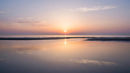 Obraz premium The sun sets over the ocean, casting a warm glow and reflecting on the calm water