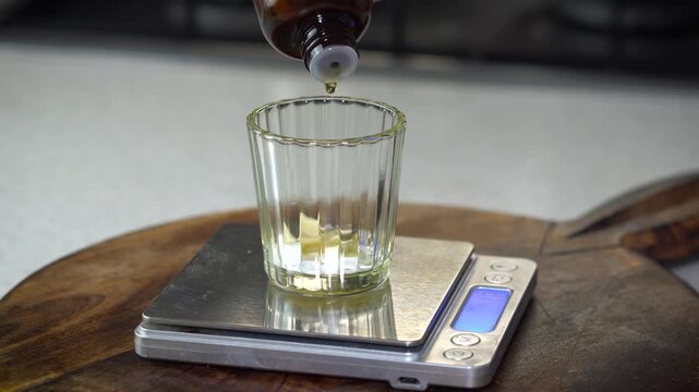 Measuring oil on digital scale for homemade lip balm. DIY natural cosmetics process with organic skincare ingredients, eco-friendly beauty preparation, and handcrafted apothecary style.