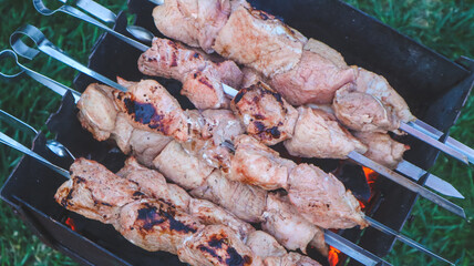 Shashlik on skewers is being cooked on charcoal in a barbecue close-up.
