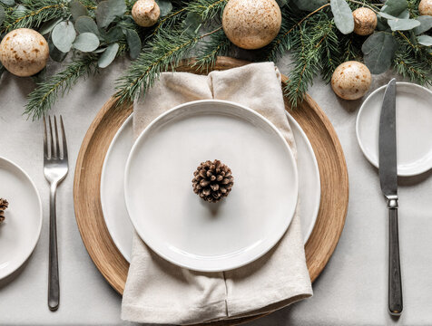 Natural Christmas dining flat lay with eco-friendly white plates, pine branches, pinecones, and rustic festive decoration