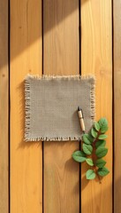 Burlap fabric with frayed edges on a wooden surface, accompanied by a wooden pen and a fresh green leafed twig