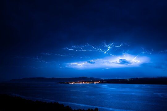 Lightning over the sea at night during a summer storm, with distant city lights. Perfect for science, design, education, media, travel, or nature visuals.
