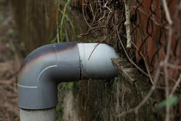 Close-up of a burnt PVC plastic pipe joint attached to an old wall next to a rusty chain-link fence, showing urban decay.